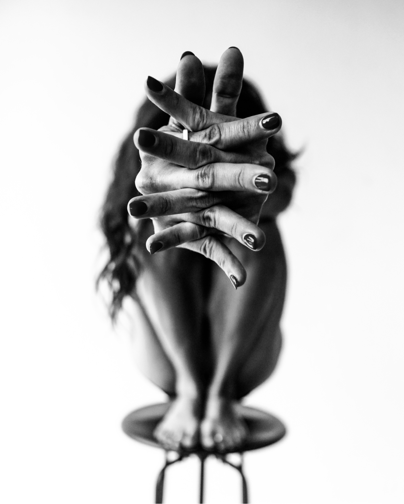 Black and white study of interlaced hands reaching toward the camera, the dancer's figure blurred behind them