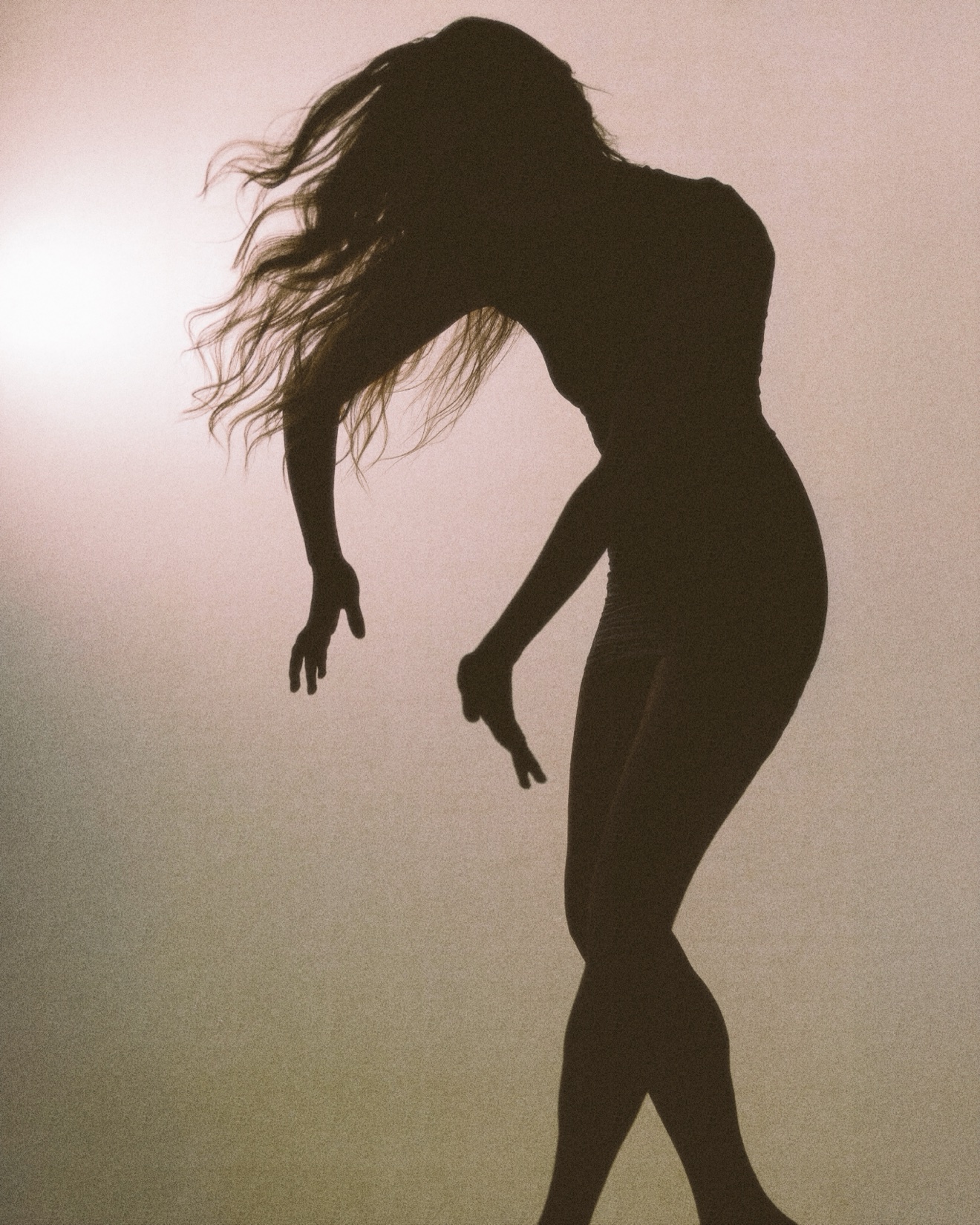 Backlit silhouette of a dancer bending forward, hair falling, against a hazy amber background